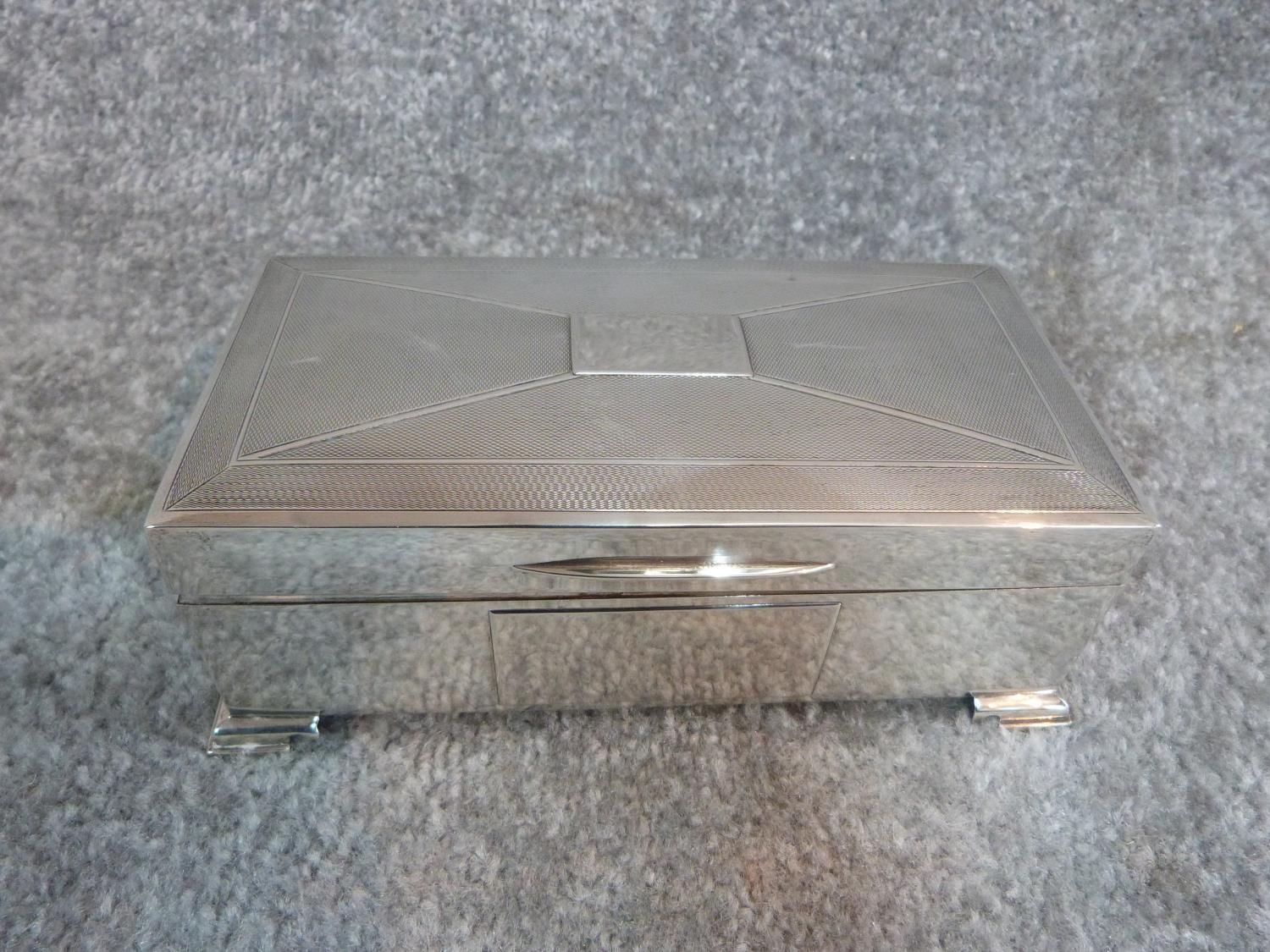 A silver cigarette box with engine turned decoration and two plain rectangular cartouches.