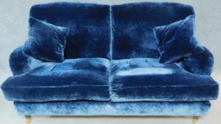 A Howard style blue velvet sofa raised on turned supports with casters. H.90 W.180 D.100cm