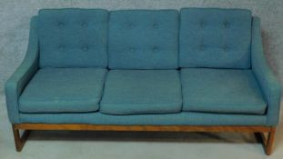 A mid 20th century teak framed sofa upholstered in turquoise raised on stretchered square