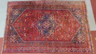 A Persian rug with central pendant medallion on a rouge field with stylised geometric borders,