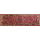 A Persian Malayer style runner with repeating floral and petal motifs on a rouge field, fringed