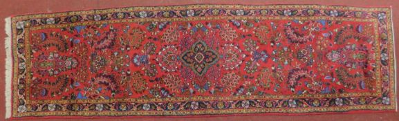 A Persian Malayer style runner with repeating floral and petal motifs on a rouge field, fringed