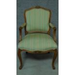 A Victorian oak armchair with floral carved details and green stripped upholstery, raised on