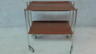 A vintage chrome framed two tier folding drinks trolley with moulded laminate teak effect shelves.