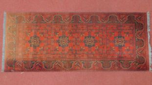 A 20th century Persian runner with four geometric medallions, on a terracotta ground, contained by