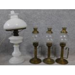 A milk glass converted oil lamp together with a set of three other brass detailed glass oil lamps.