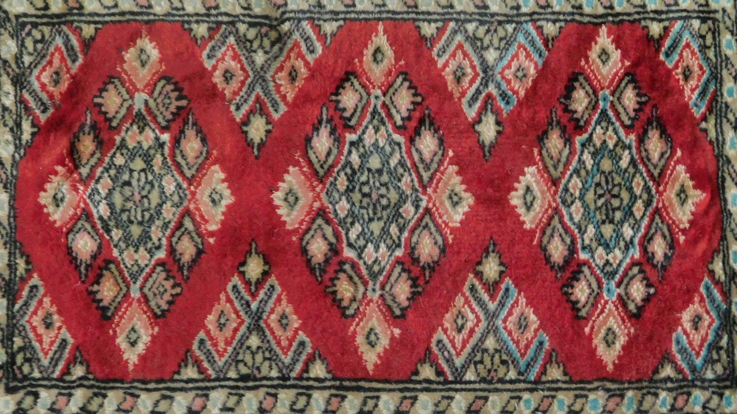 A Persian rug with triple pendant medallions, set on a rouge field with repeating geometric motifs - Image 2 of 4