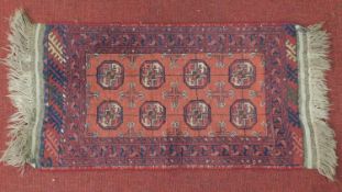 A Bokhara style rug with elephant pad motifs on a rouge field, within border with petal motifs.