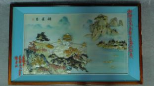 A framed and glazed Chinese abalone shell artwork depicting a temple on top of one of two mountains.