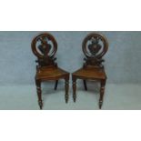 A pair of Victorian oak hall chairs with carved floral shield backs, raised on tapering turned