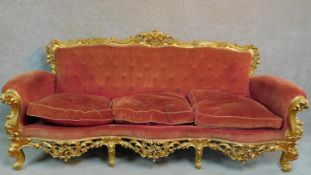 An Italian Rococo style carved giltwood sofa in buttoned rouge upholstery raised on cabriole legs.