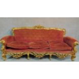 An Italian Rococo style carved giltwood sofa in buttoned rouge upholstery raised on cabriole legs.