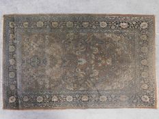 A Persian rug with floral motifs on a brown field surrounded by floral borders and fringed, worn