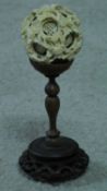 An antique ivory puzzle ball on a carved pierced Chinese hardwood stand. The puzzle ball has a