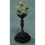 An antique ivory puzzle ball on a carved pierced Chinese hardwood stand. The puzzle ball has a