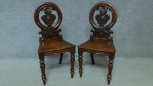 A pair of Victorian oak hall chairs with carved floral shield backs, raised on tapering turned