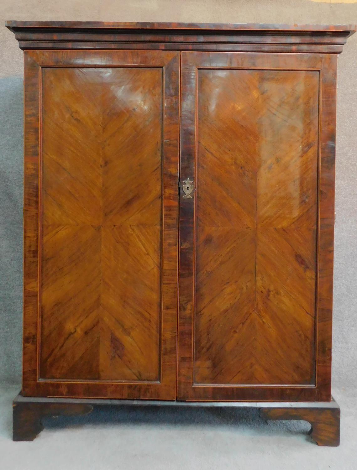 A Georgian mahogany press cupboard with quarter veneered and crossbanded panel doors enclosing
