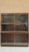 A Mid 20th century mahogany three section bookcase fitted sliding glass doors on plinth base, by