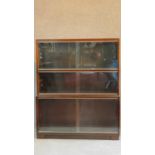 A Mid 20th century mahogany three section bookcase fitted sliding glass doors on plinth base, by
