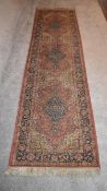 A Persian runner with triple pole medallion on a rouge background and floral border. L.273 x 73cm
