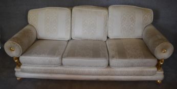 A three seater sofa with cream upholstery and gilt metal lion supports to the arm rests on claw