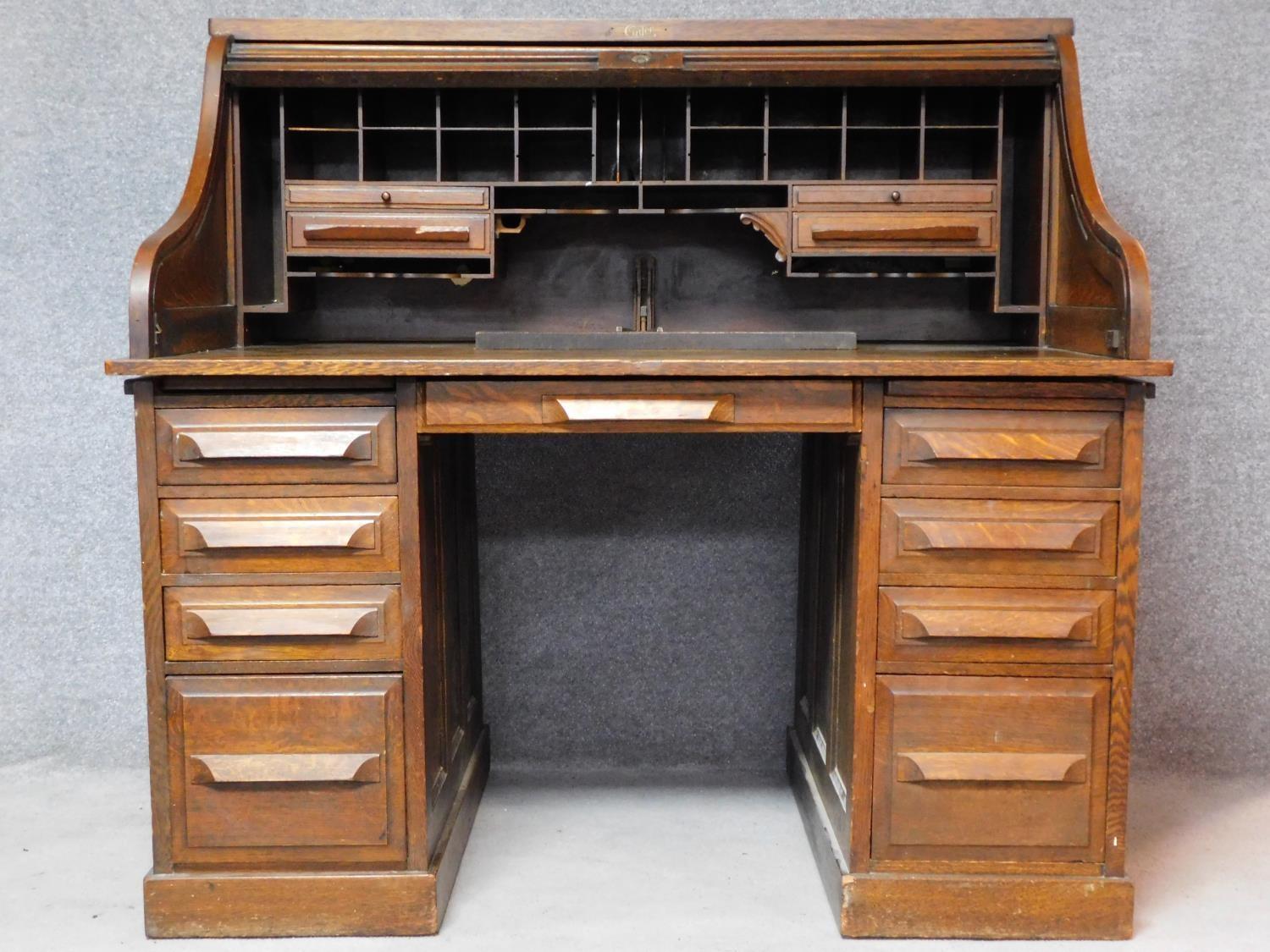 A late 19th century oak roll top desk with tambour shutter enclosing fitted interior above an