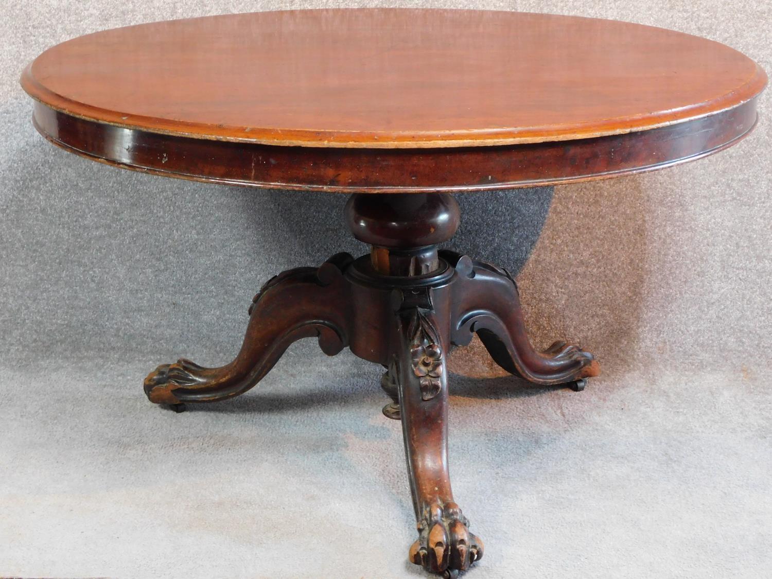 An early Victorian mahogany circular tilt top loo table raised on carved tripod base with lion paw