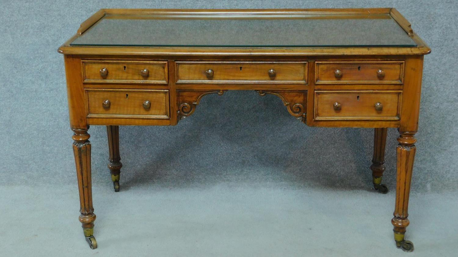 A William IV mahogany writing table with glass inset top and five frieze drawers, raised on tapering