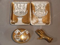 A collection of Fornasetti ceramics and a brass hand paperweight. The pebble paperweight has a