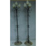 A pair of wrought iron floor standing three branch candelabras with four opaque glass shades in