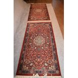 A pair of Keshan rugs with central floral medallions on a rouge field with multi stylised floral