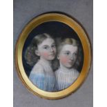 An oval framed pastel portrait of two young girls posing together, unsigned. 65x57cm