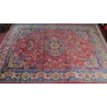 A large Persian Tabriz style rug with central double pendant medallion on a rouge field framed