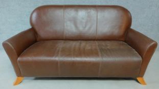 A shaped back two seater sofa in tan leather upholstery on swept supports. H.87 W.170 D.77cm