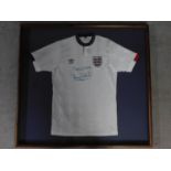 A framed and glazed official England shirt, signed, Terry Butcher. 99x106cm