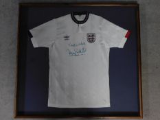 A framed and glazed official England shirt, signed, Terry Butcher. 99x106cm