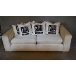 A three seater sofa upholstered in cream fabric and cushions printed with Japanese script. H.70 x