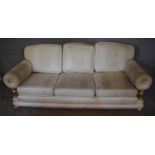 A three seater sofa with cream upholstery and gilt metal lion supports to the arm rests on claw