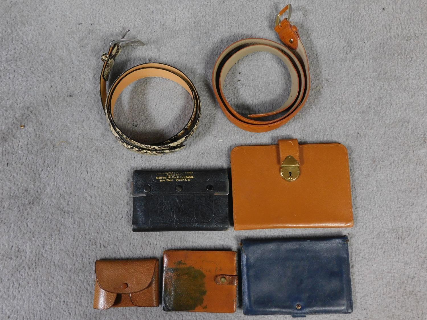 A collection of vintage leather travel and money wallets and two belts. One belt is ostrich and