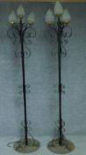 A pair of wrought iron floor standing three branch candelabras with four opaque glass shades in