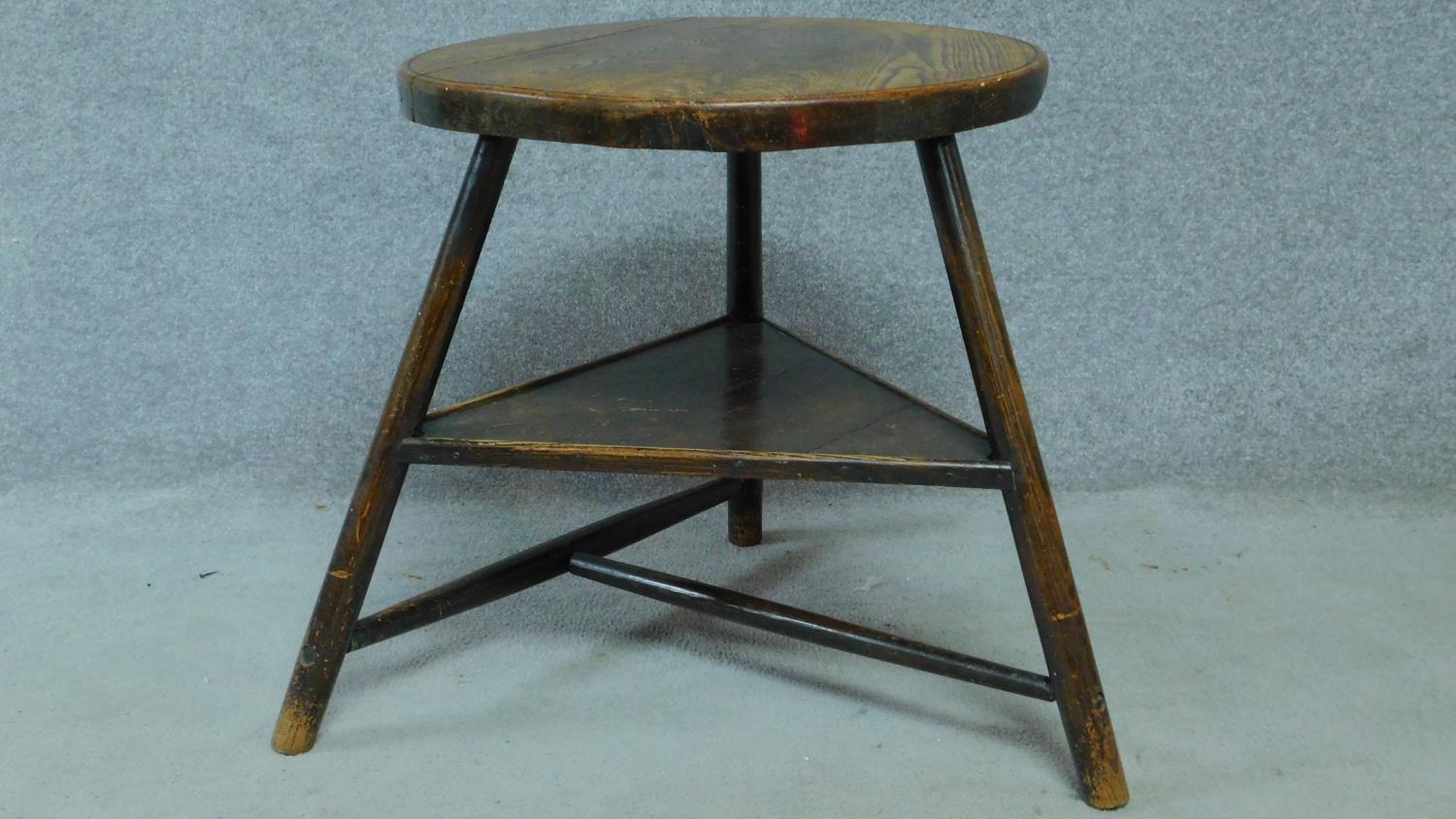 An antique elm circular topped cricket table on three circular section splayed supports united by