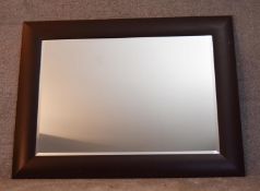 A large bevelled edge wall mirror in ebonised cushion frame. H.92x120cm