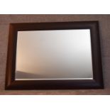 A large bevelled edge wall mirror in ebonised cushion frame. H.92x120cm