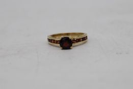 A vintage 9ct yellow gold and garnet flanked solitaire ring. Set to centre with a round mixed cut