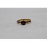 A vintage 9ct yellow gold and garnet flanked solitaire ring. Set to centre with a round mixed cut