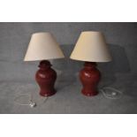A large pair of deep red glazed table lamps of bulbous form with cream shades. H.80cm (inc. shade)