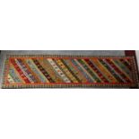 A brightly coloured runner with repeating geometric design surrounded by stylised borders 256x62cm