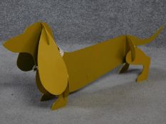 A metal painted sculpture of a sausage dog with a collar to its neck by British artist Peter