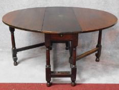 An antique country oak drop flap dining table with frieze drawer and gateleg action on turned