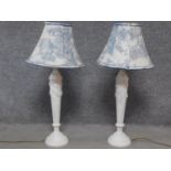 A pair of vintage white carved table lamps with blue and white shades. Bases have relief bow and